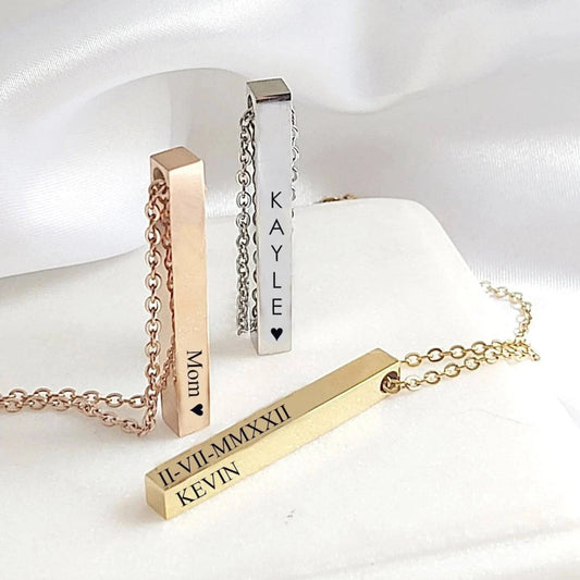 Three vertical bar necklaces with engraved names on a white fabric background