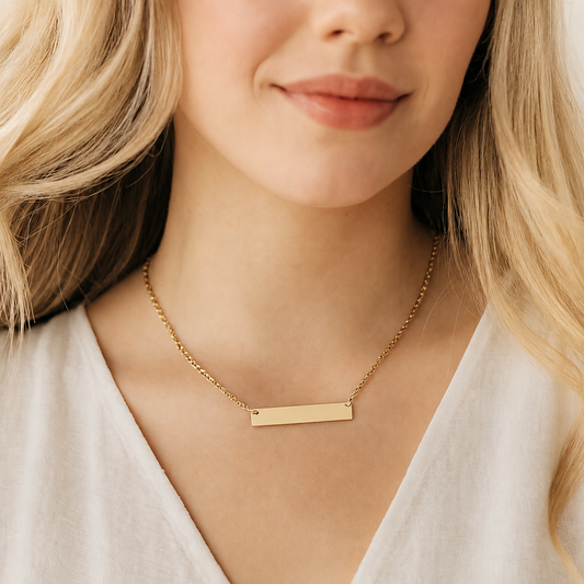 Woman wearing a polished gold-tone stainless steel horizontal bar necklace with a delicate matching chain. The rectangular bar pendant is shown blank and ready to be personalized with a name, date, initials, message or meaningful design.