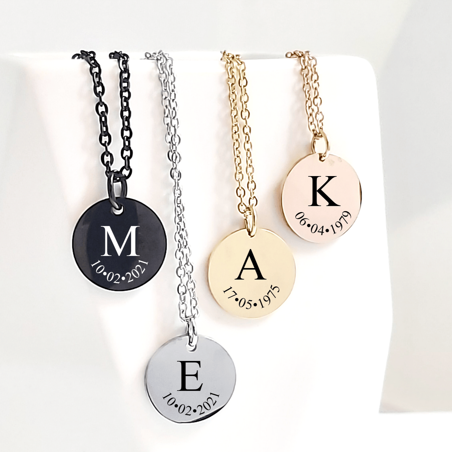 Four necklaces with engraved letters and dates on a white background