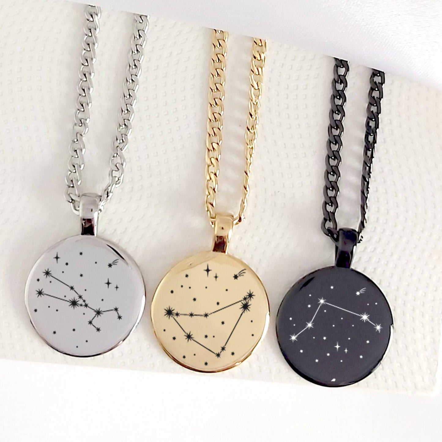 Three necklaces with star constellation pendants on a textured white surface