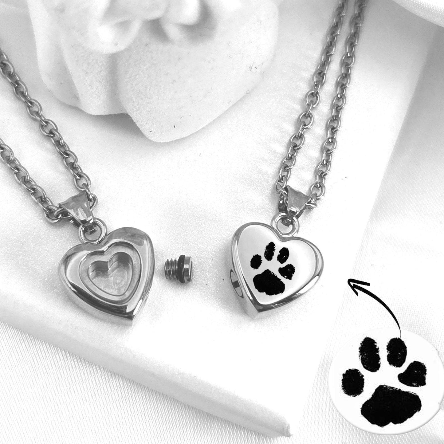 Two silver heart-shaped urn pendants with paw prints on a white surface.