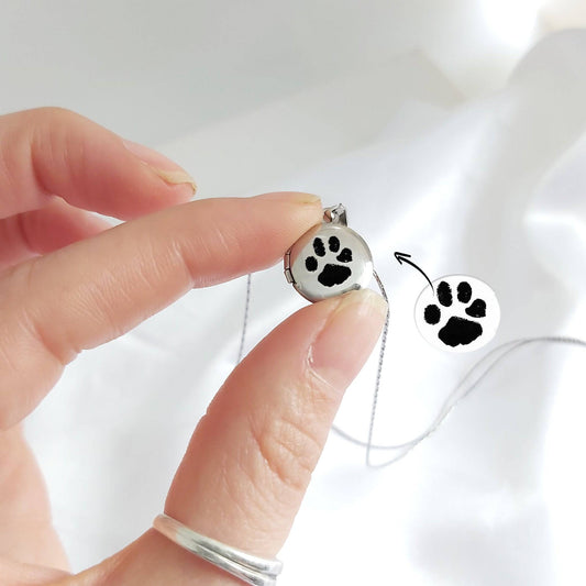 Hand holding a tiny locket necklace engraved with a paw print