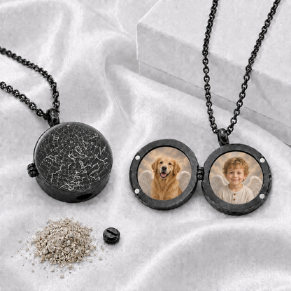 Two round black memorial urn lockets with matching black chains on white fabric. One closed locket features an engraved white star map. The second is open and displays circular photos of a golden dog and a young child with angel wings. A small black screw and symbolic ashes are shown below.
