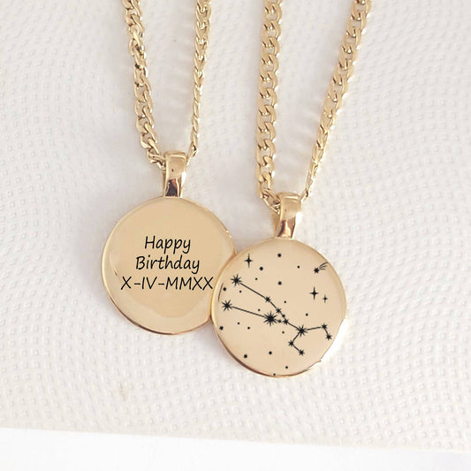 Two gold necklaces with circular pendants, one engraved with 'Happy Birthday' and a date, the other with a constellation design, on a textured white background.