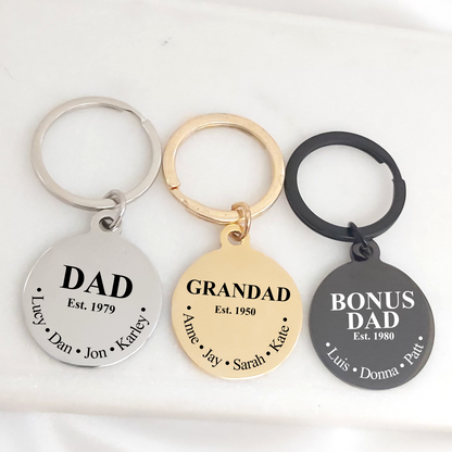 Three round stainless steel keychains in silver, gold, and black finishes engraved with “Dad,” “Grandad,” and “Bonus Dad,” along with established years and children’s names. Each 25mm pendant features a polished finish and hangs from a matching key ring, displayed on a white background. Available in silver, gold, and black, with front and back engraving options and elegant gift packaging.