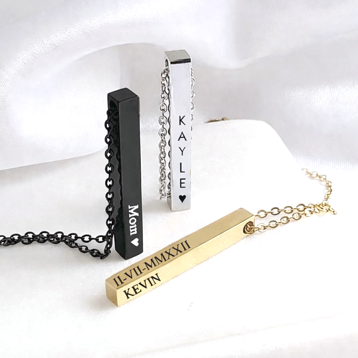 Four bar-shaped necklaces with engraved names on a white fabric background
