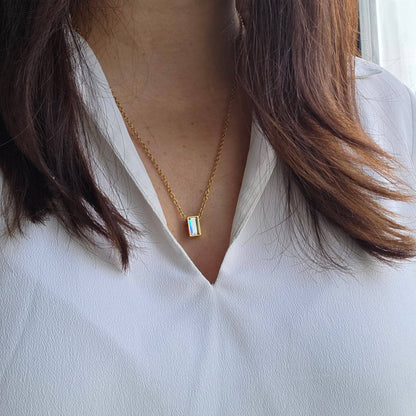 Gold necklace with a rectangular pendant worn by a person in a white shirt.