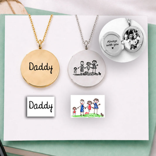 Two necklaces with engraved text on a green book with a pen and cards on a white satin background