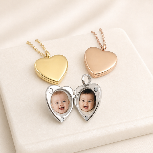 Three polished heart-shaped locket necklaces displayed on a soft ivory surface: a closed gold locket, a closed rose gold locket, and an open silver-tone locket holding two baby photos. Each stainless steel heart pendant has a coordinating chain and smooth, blank front ready for personalization.