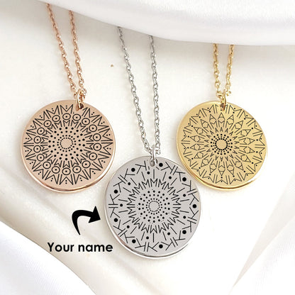 Two gold stainless steel necklaces with round 20mm pendants engraved with intricate mandala designs created from personalized names. Each hangs from an adjustable 18–20 inch chain, displayed on a white background. Available in silver, gold, and black finishes, with optional back engraving and elegant gift packaging.