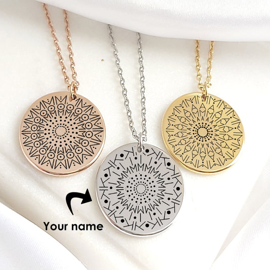 Two gold stainless steel necklaces with round 20mm pendants engraved with intricate mandala designs created from personalized names. Each hangs from an adjustable 18–20 inch chain, displayed on a white background. Available in silver, gold, and black finishes, with optional back engraving and elegant gift packaging.