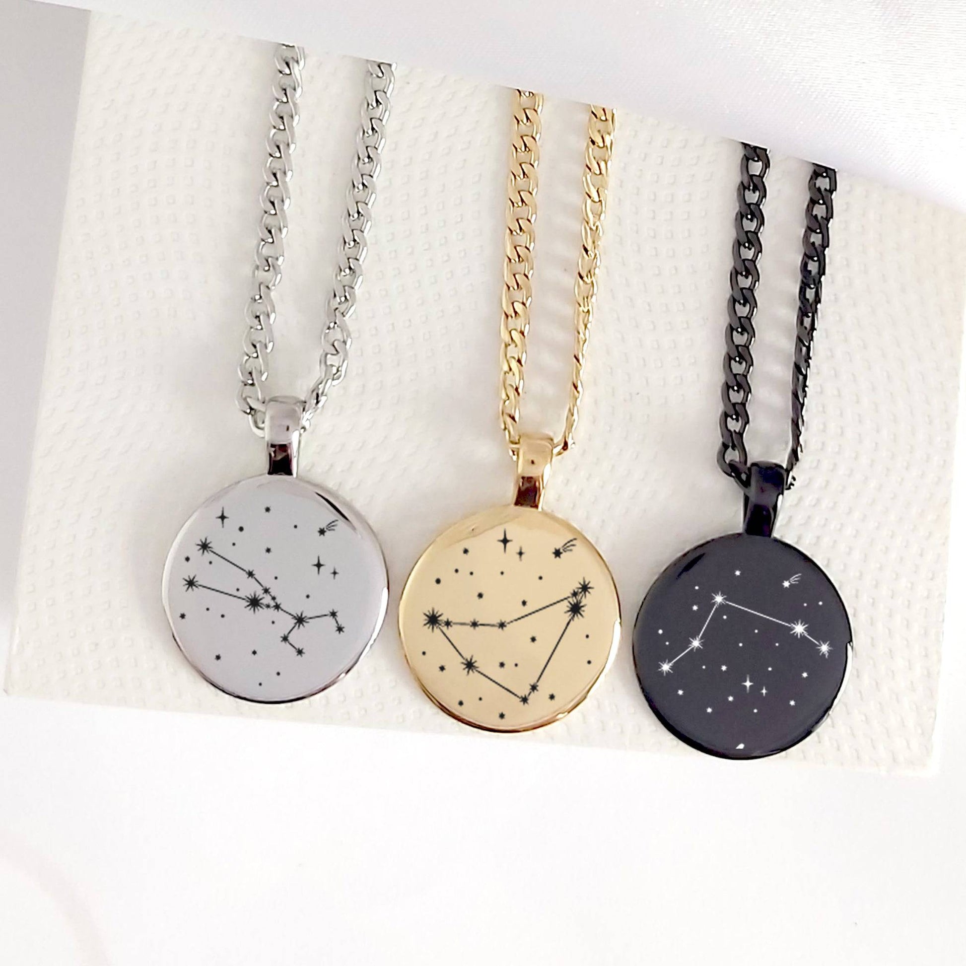 Three necklaces with star constellation pendants on a textured white surface