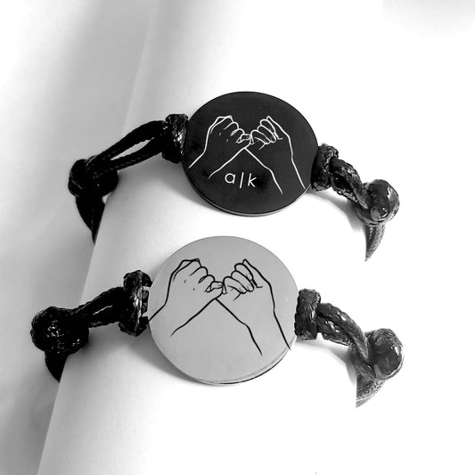 Black bracelet with circular charm featuring pinky promise sign