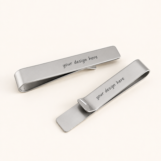 Two polished silver-tone rectangular tie clips displayed diagonally on a warm ivory background. Each stainless steel tie clip features rounded ends and the black personalized text “your design here” across the front.