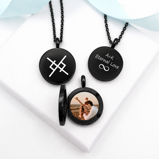 Three round black lockets with matching black chains on white fabric. One closed locket features a white geometric Viking symbol, another is engraved with “A+K Eternal Love” and an infinity symbol, and the open locket displays a color photograph of a couple.
